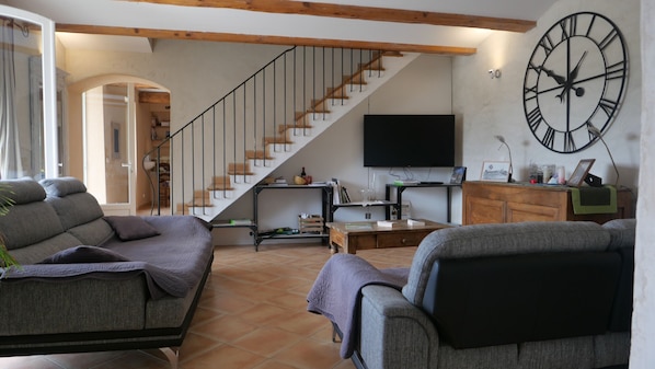 A living room with a staircase, a large wall clock, and a flat-screen TV.