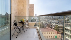 A balcony with a table and chairs, a view of the cityscape, and a building with a stone facade.