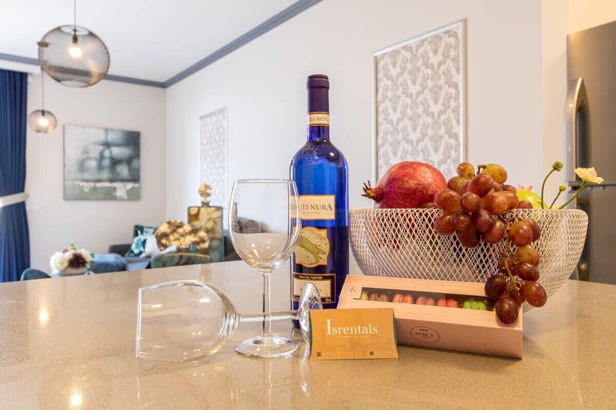 Uma mesa com uma garrafa de vinho, uma taça, uma tigela de uvas e uma caixa de frutas.