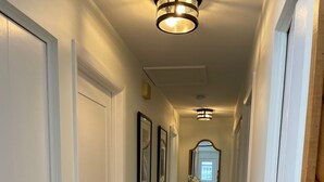 A hallway with white doors, framed pictures, a rug, and a mirror.