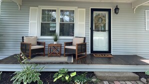 A porch with two wicker chairs, a small table, and a potted plant.