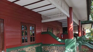 Een rood en groen houten gebouw met een overdekte veranda, een stenen muur en groene stoelen.