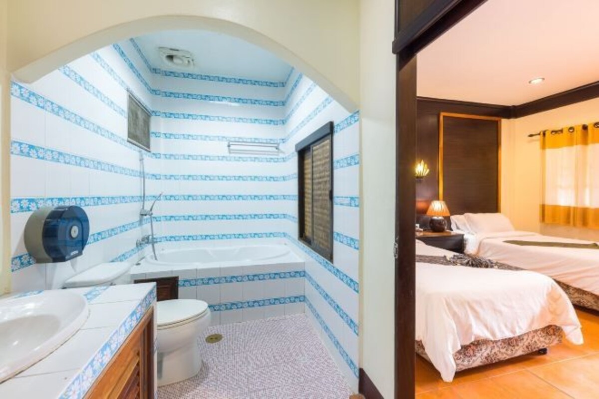 Een badkamer met bad, toilet en wastafel, en een slaapkamer met twee bedden en een nachtkastje.