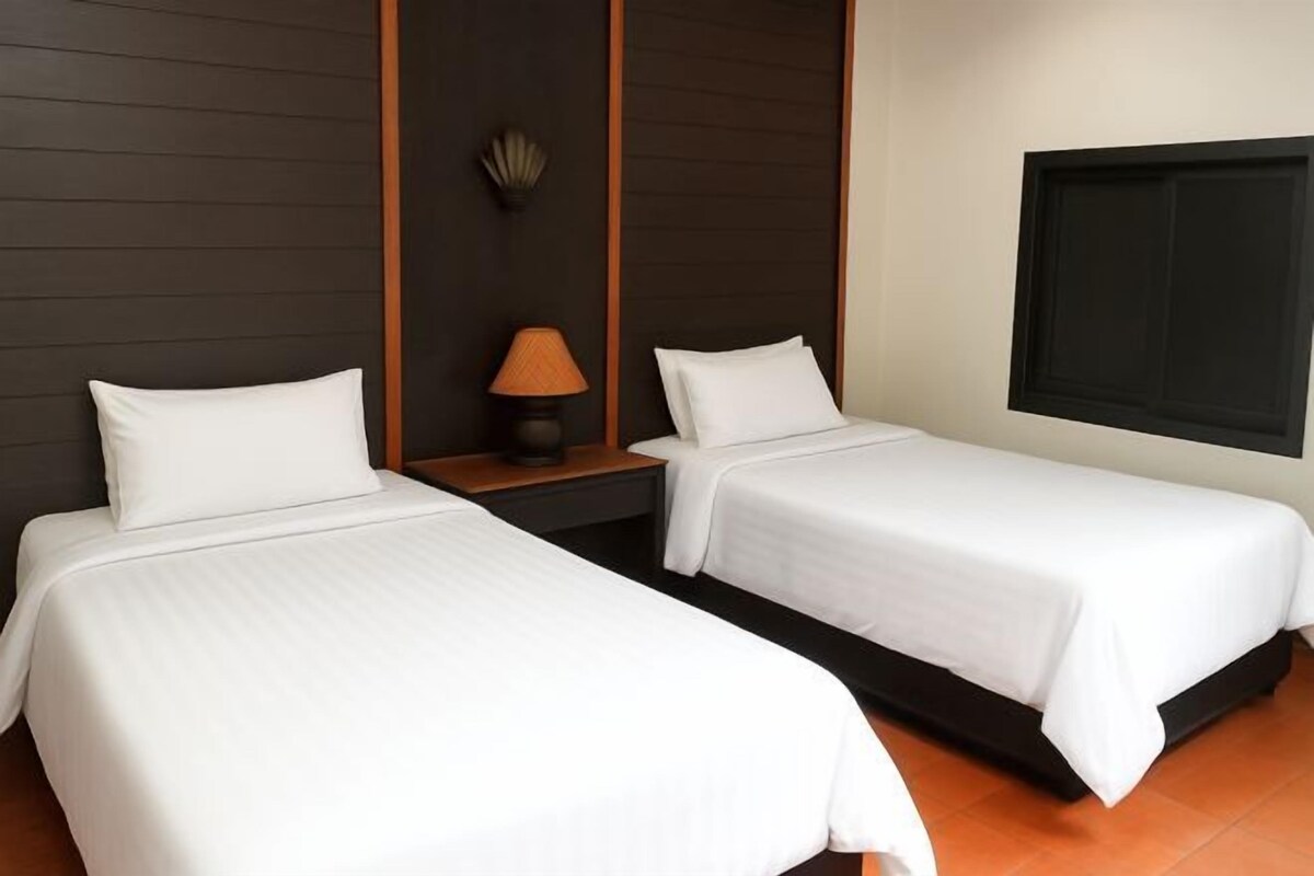 Habitación de hotel con dos camas individuales, una mesita de noche con lámpara y un ventanal grande.