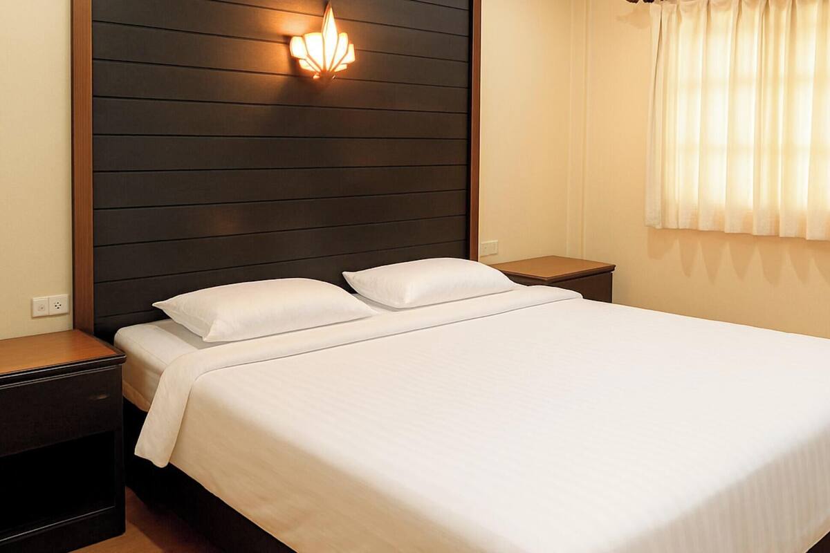 A hotel room with a bed, two bedside tables, a wall-mounted light, and a window with curtains.