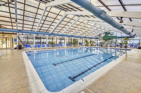 An indoor swimming pool with clear lanes, blue lounge chairs, and a high ceiling with a skylight.