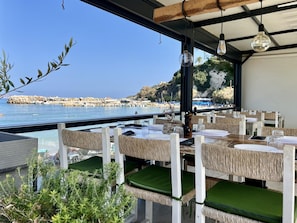 Un espace extérieur aménagé pour les repas, avec des tables et des chaises, offrant une vue sur une plage et une côte rocheuse.