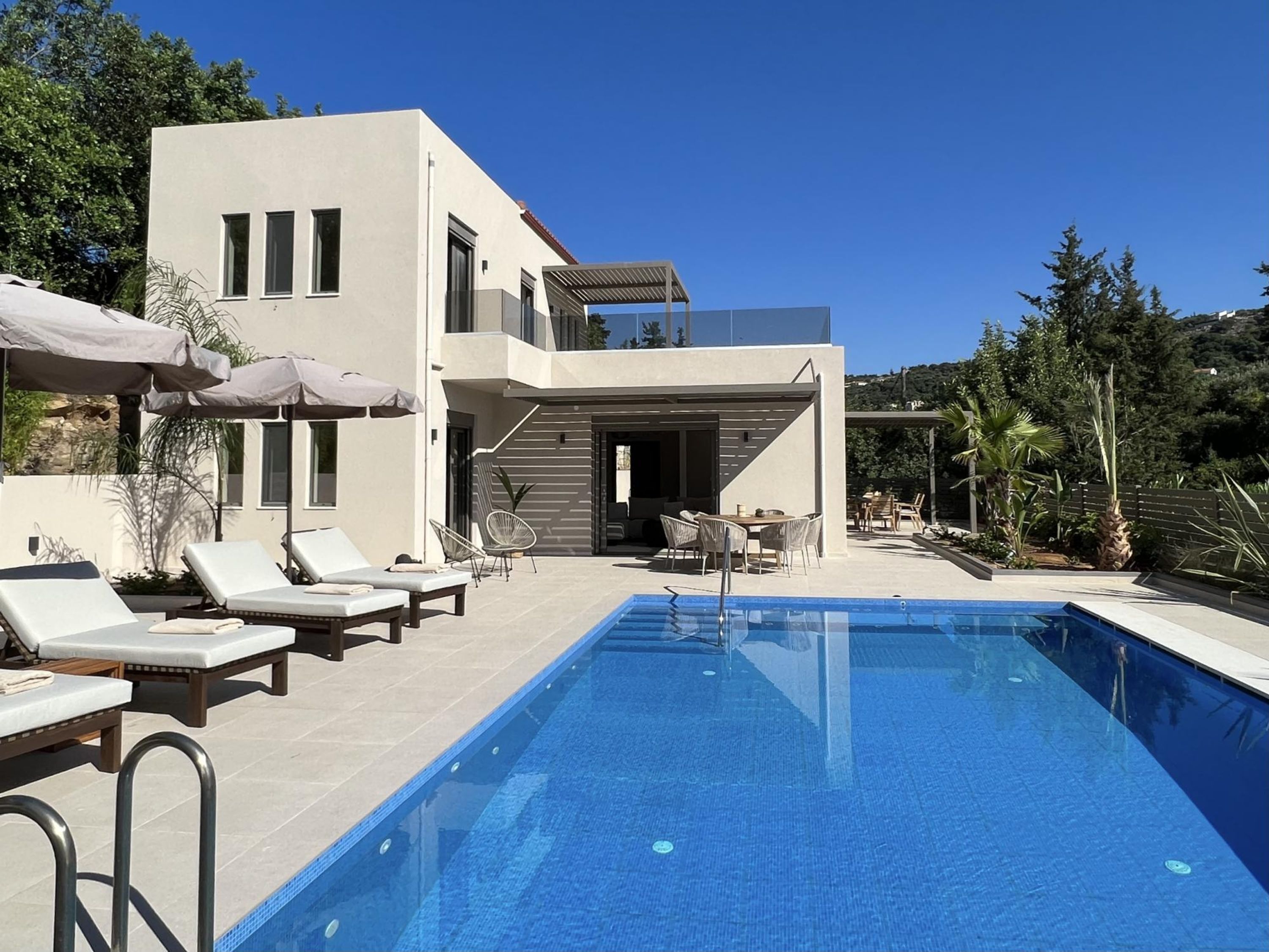 A modern house with a swimming pool, lounge chairs, and a patio area.