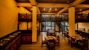 A restaurant with wooden tables and chairs, a high ceiling with decorative elements, and large windows allowing natural light. - Amritara Hidden Land, Gangtok (Gangtok)