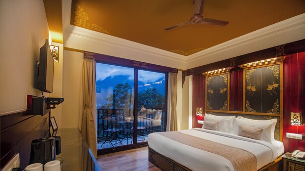 A hotel room with a large bed, a desk with a telephone, and a balcony with outdoor furniture. - Amritara Hidden Land, Gangtok (Gangtok)