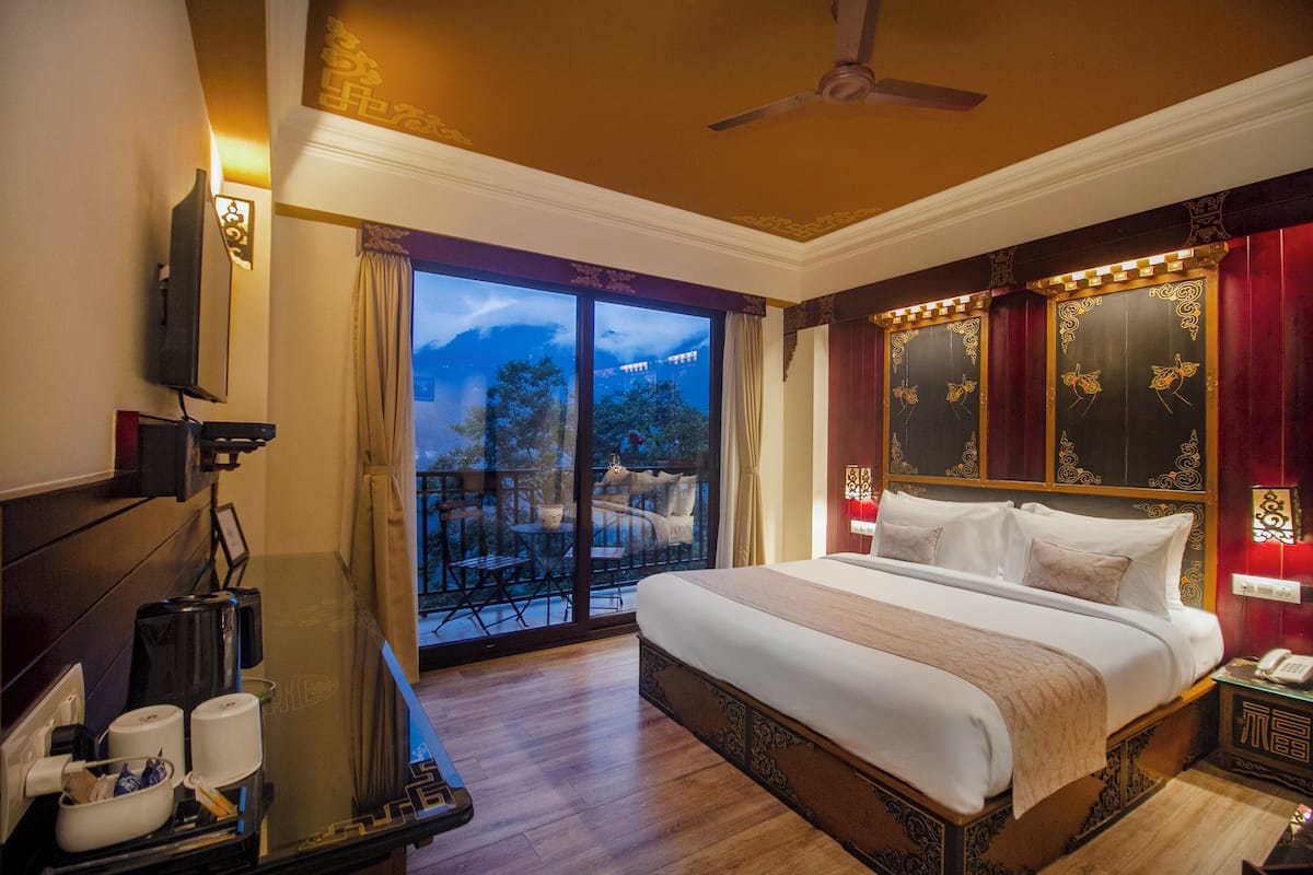 A hotel room with a large bed, a desk with a telephone, and a balcony with outdoor furniture.