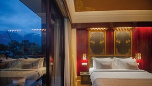 A hotel room with a large bed, a sitting area with a table and chairs, and a view of mountains through the window. - Amritara Hidden Land, Gangtok (Gangtok)