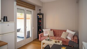 Ett kompakt bostadsutrymme med ett litet kök, en rosa soffa, ett matbord och en bokhylla.