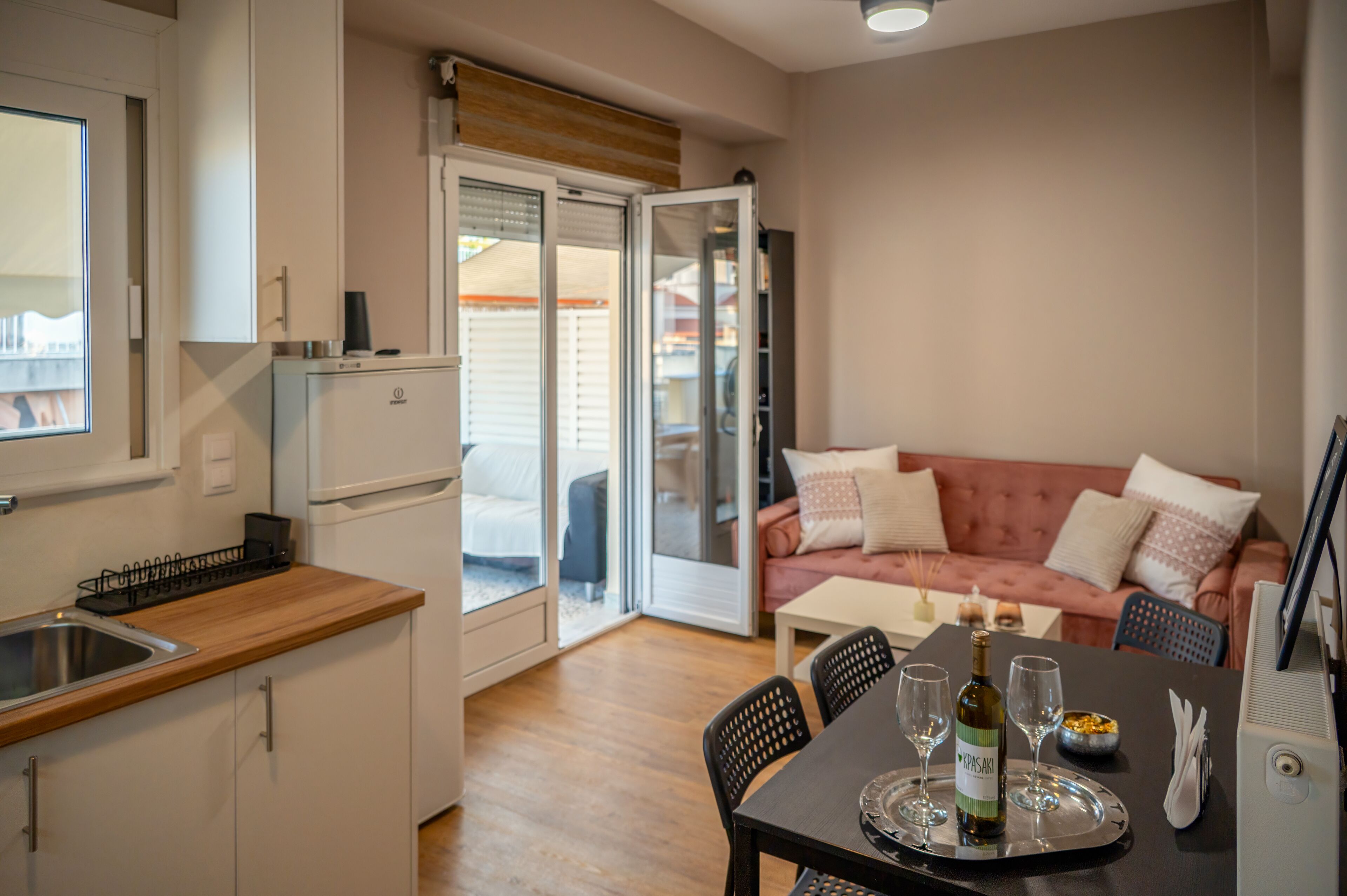 A compact kitchen with a sink and cabinets, a dining area with a table set for two, and a cozy living area with a sofa and cushions.