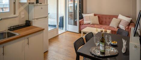 A compact kitchen with a sink and cabinets, a dining area with a table set for two, and a cozy living area with a sofa and cushions.
