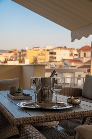 A table set with two wine glasses and a bottle on a balcony overlooking a cityscape. - Acropolis Terrace view apartment  (Athina)