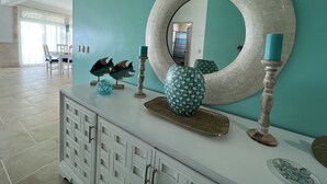 A modern interior with a teal accent wall, a round mirror, decorative fish sculptures, and a patterned vase on a white console.
