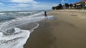 A beach with a person standing on the sand, facing the ocean.