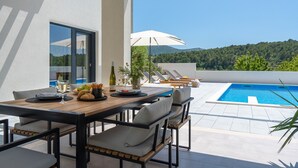 A modern outdoor dining area with a pool, overlooking a mountainous landscape. - Stylish property with heated 32sqm private pool, 3 bedrooms, 3 bathrooms, table tennis and table soccer (Gata)