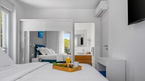 A modern hotel room with a bed, a bedside table with a tray of fruits and a glass of orange juice, a bathroom with a sink and mirror, and a TV mounted on the wall. - Stylish property with heated 32sqm private pool, 3 bedrooms, 3 bathrooms, table tennis and table soccer (Gata)