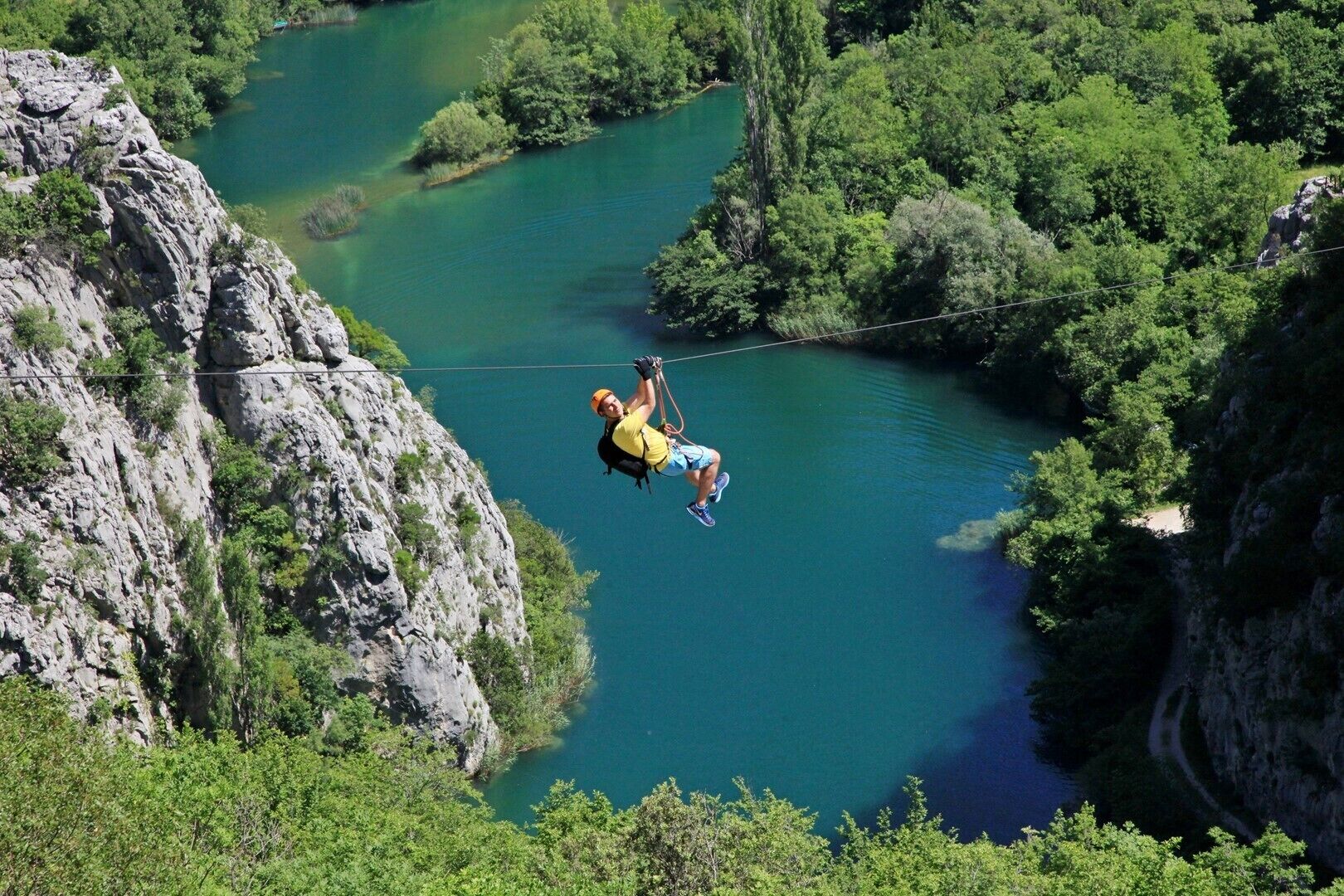 A person bungee jumping from a cliff over a river surrounded by greenery.