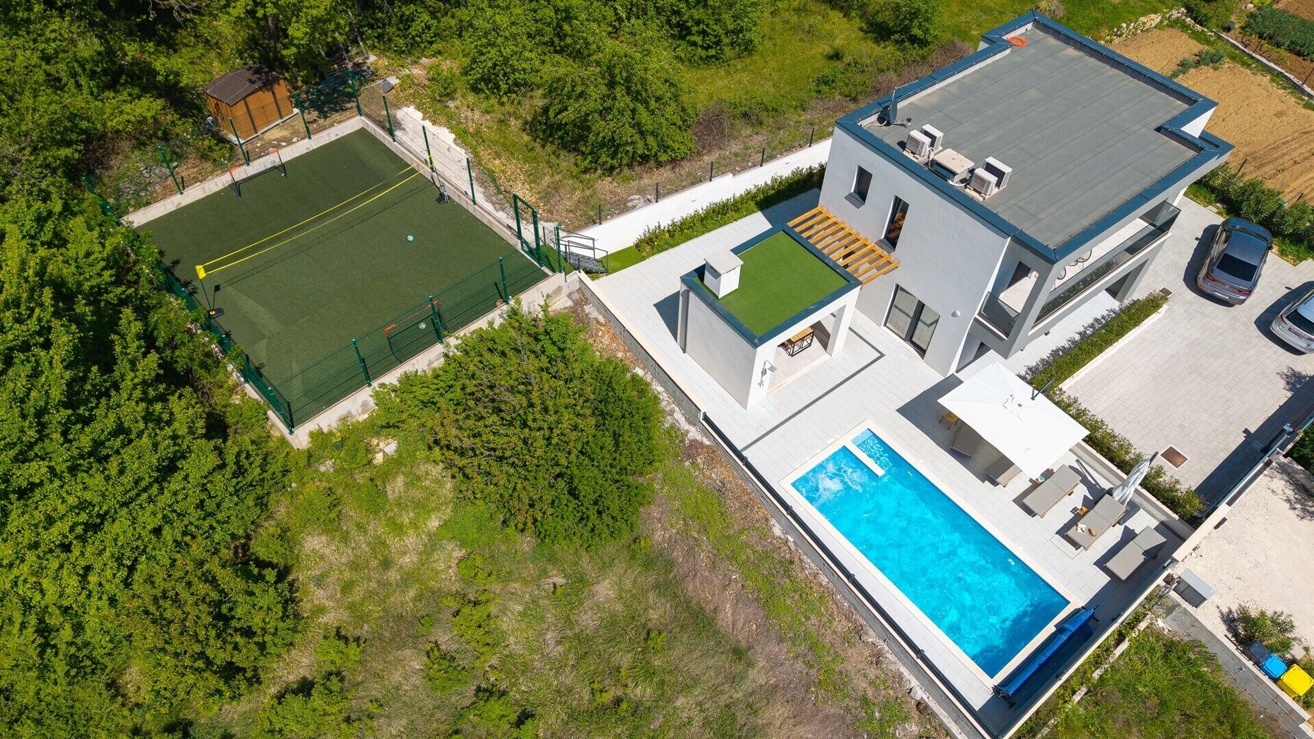 A modern two-story house with a rooftop terrace, a swimming pool, and a tennis court.