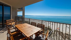 A balcony with a wooden table and chairs, overlooking a beach and the sea.