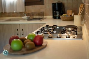 A kitchen with a gas stove, a coffee maker, and a fruit bowl with apples. - Luxury Villa Nefeli w Private Pool (Skiathos)
