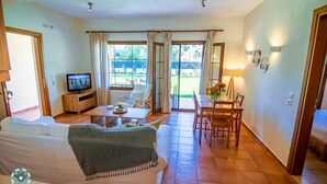A living room with a sofa, a coffee table, a TV, and a dining area with a table and chairs. - Luxury Villa Nefeli w Private Pool (Skiathos)