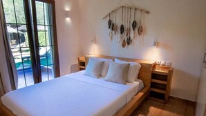A bedroom with a large bed, wooden headboard, bedside tables, and a macrame wall hanging. - Luxury Villa Nefeli w Private Pool (Skiathos)