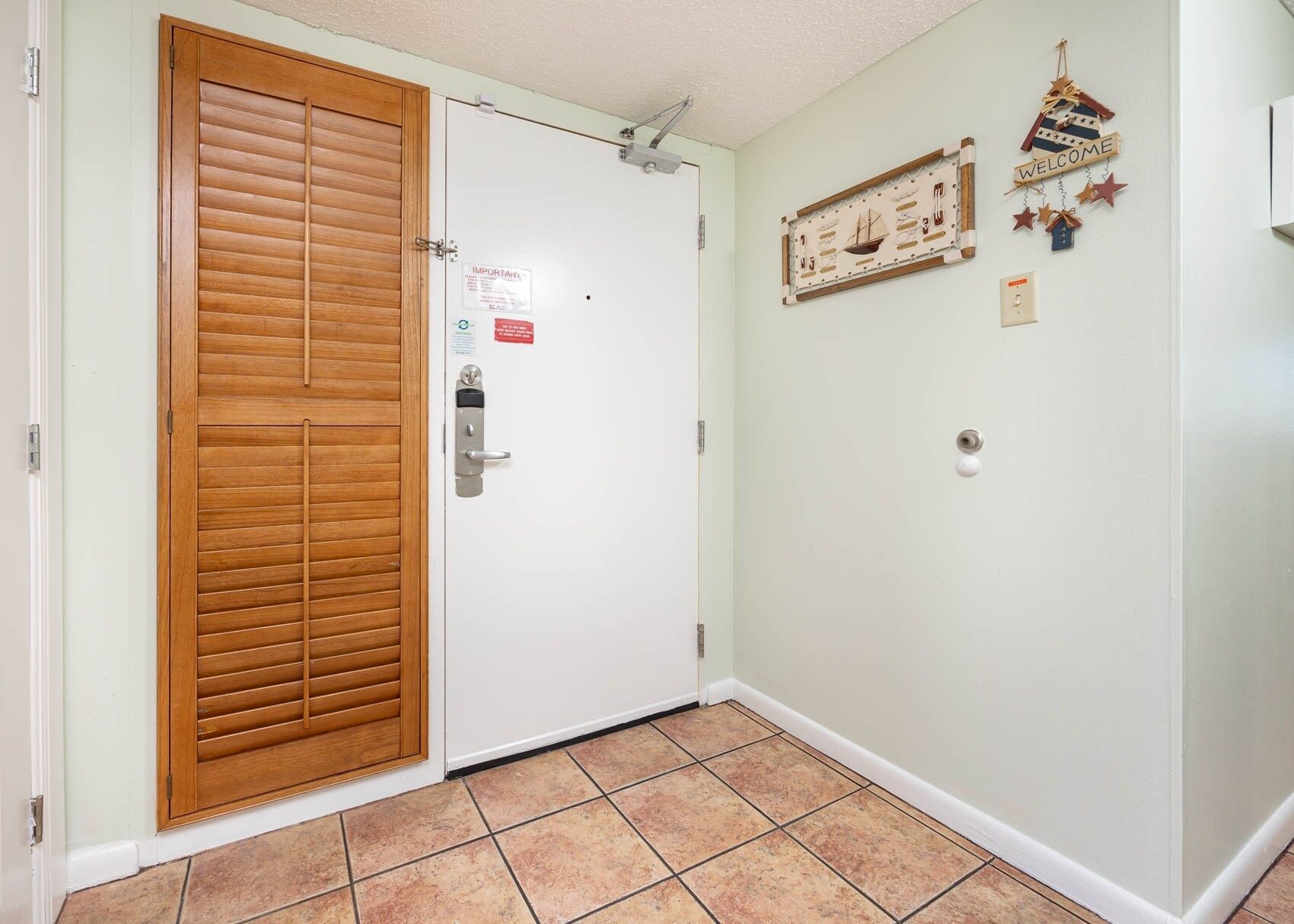 A room with a wooden sliding door, a white wall with a welcome sign, and a tiled floor.