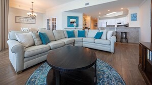 A living room with a sectional sofa, a round coffee table, and a kitchen in the background.