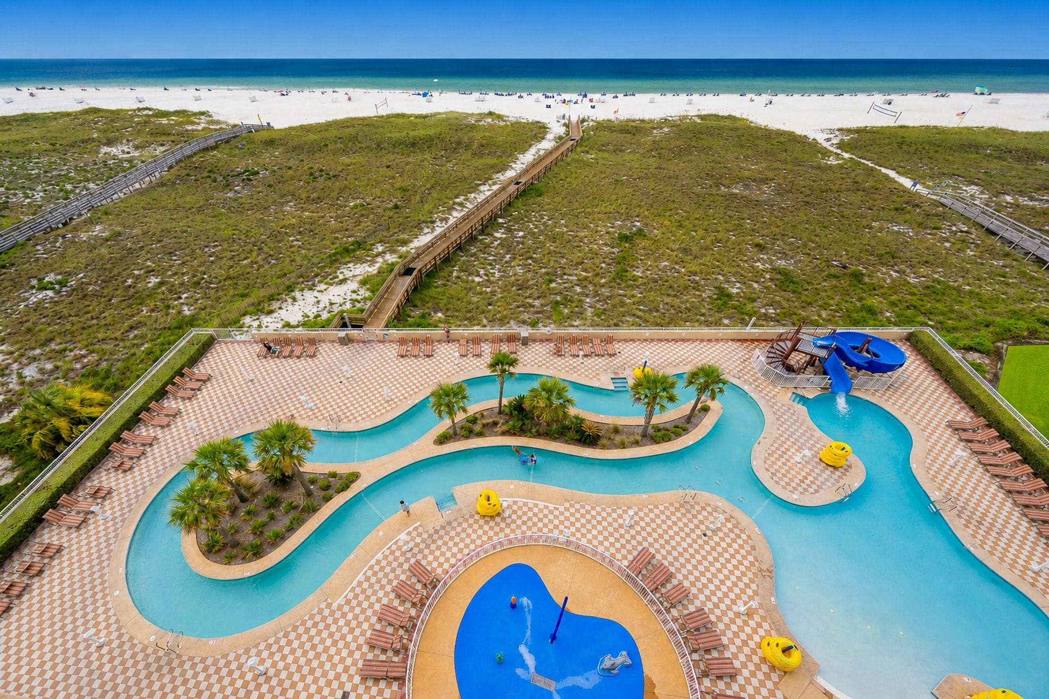 A resort with a large pool area, a beach, and a boardwalk.
