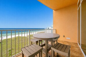 A balcony with a table and chairs, overlooking a beach and ocean.