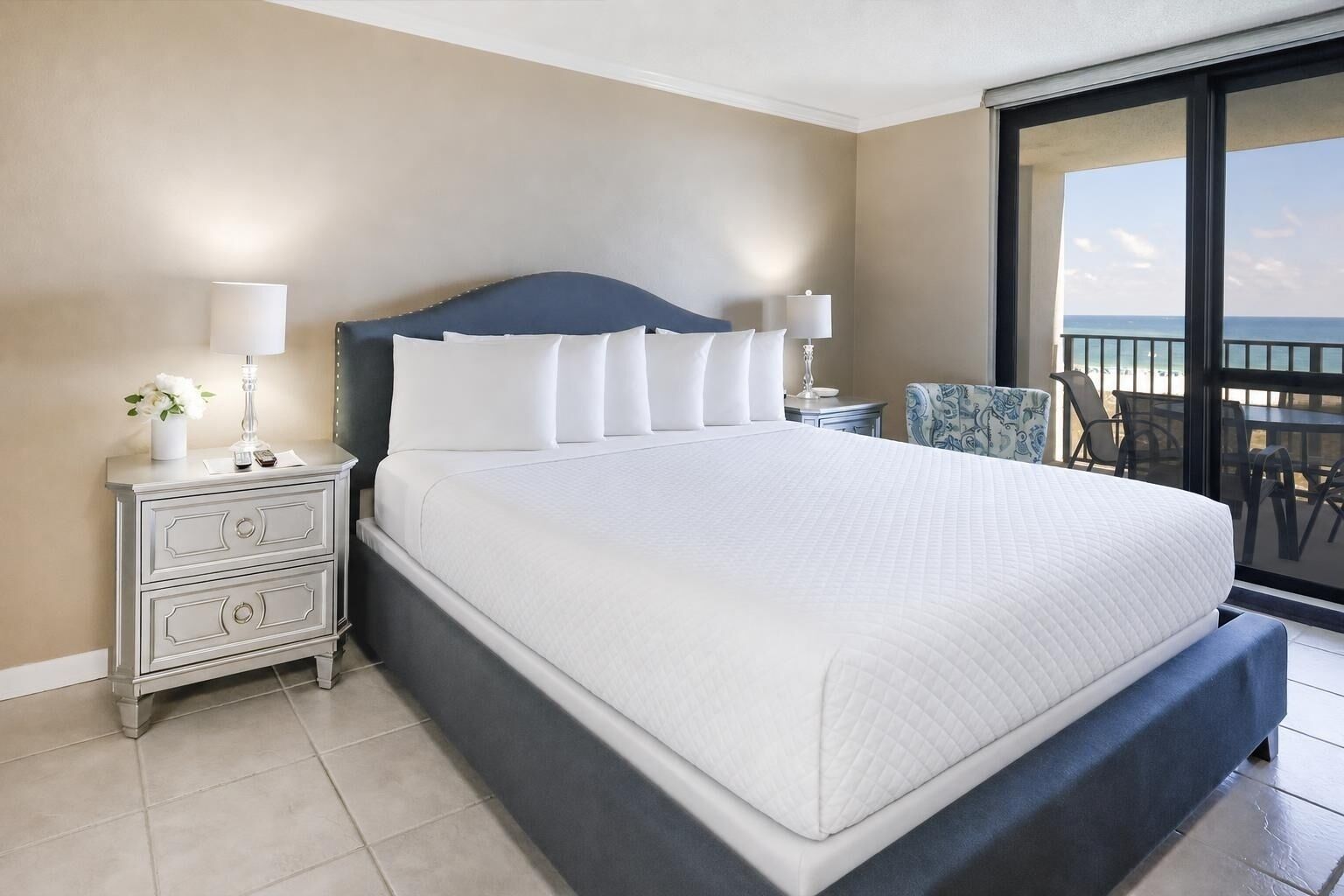 Uma cama grande com roupa de cama branca, cabeceira escura e duas mesas de cabeceira com abajures.