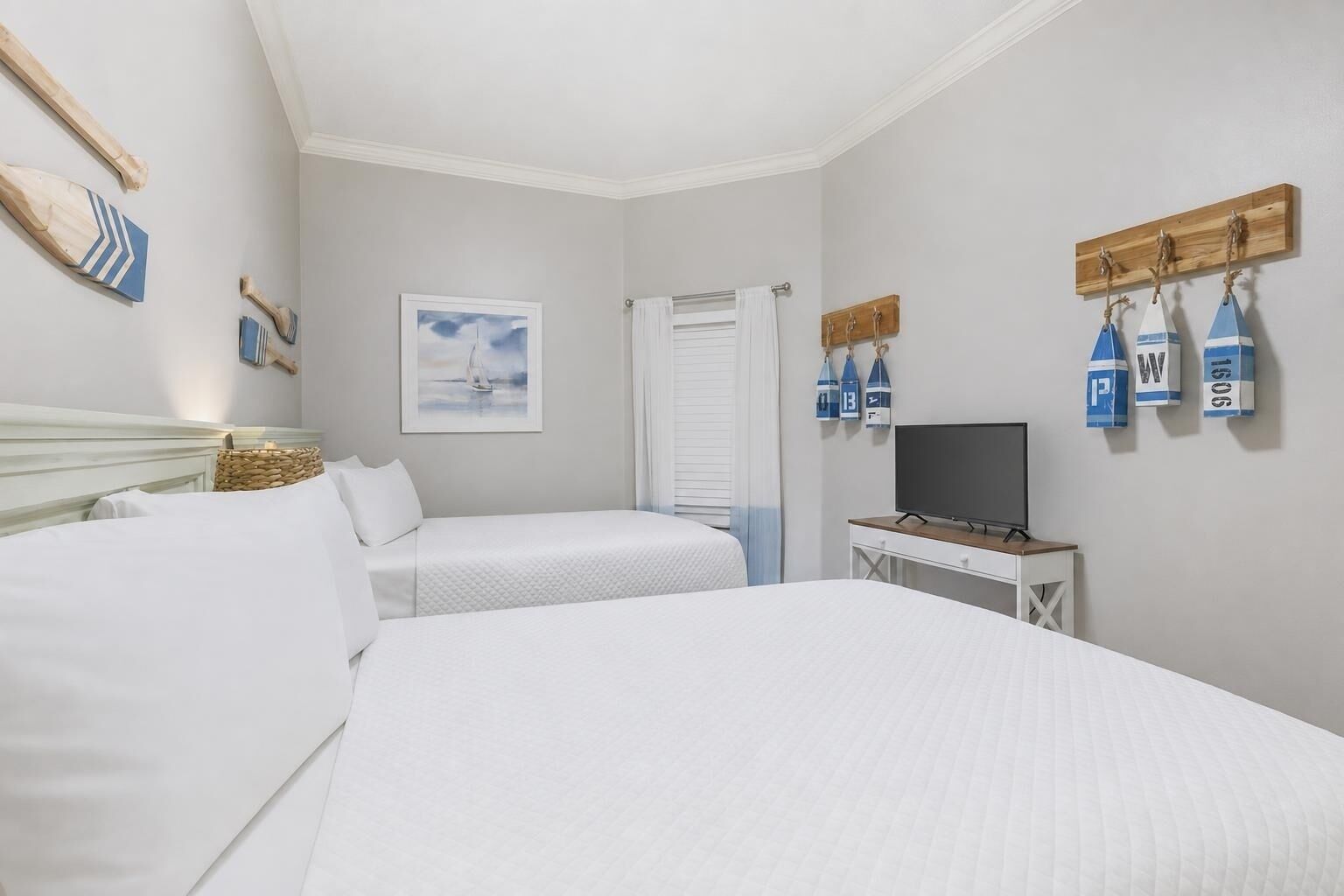 A hotel room with two beds, a television, a wooden shelf with nautical-themed decorations, and a framed picture on the wall.