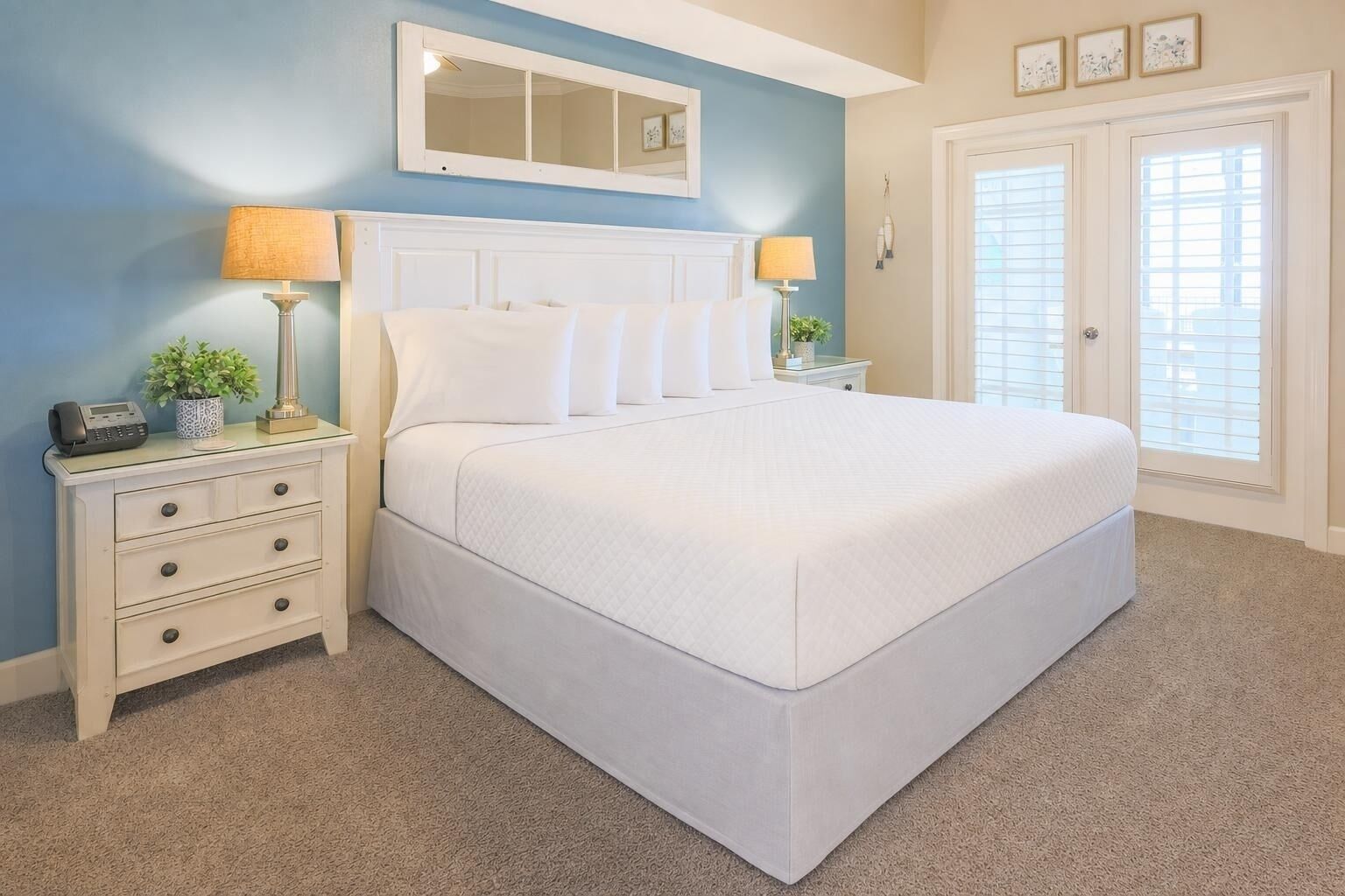 Une chambre à coucher avec un grand lit, deux tables de chevet, une commode, un miroir et une porte avec des stores.