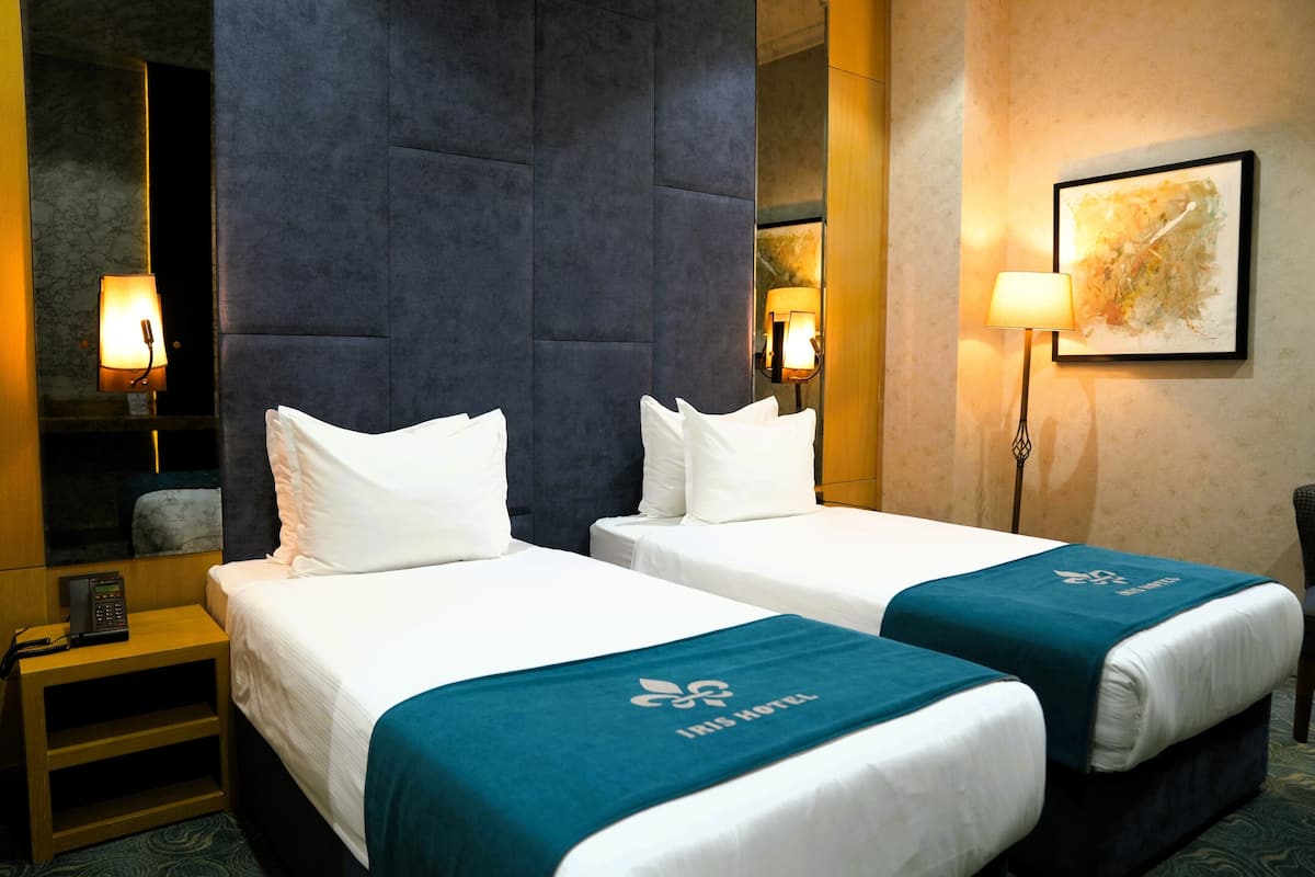 Habitación de hotel con dos camas, una mesita de noche, una lámpara y un cuadro enmarcado en la pared.