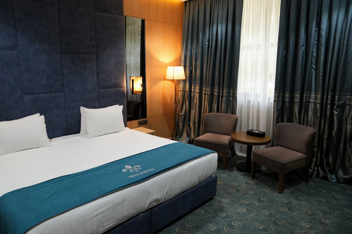 Habitación de hotel con una cama grande, un escritorio, dos sillas, una lámpara y vistas al exterior.