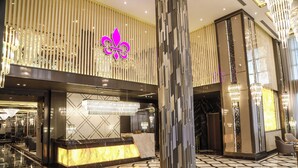 Un hall d’entrée avec un comptoir de réception, une grande colonne et un mur décoratif orné d’un motif en forme de fleur de lys.