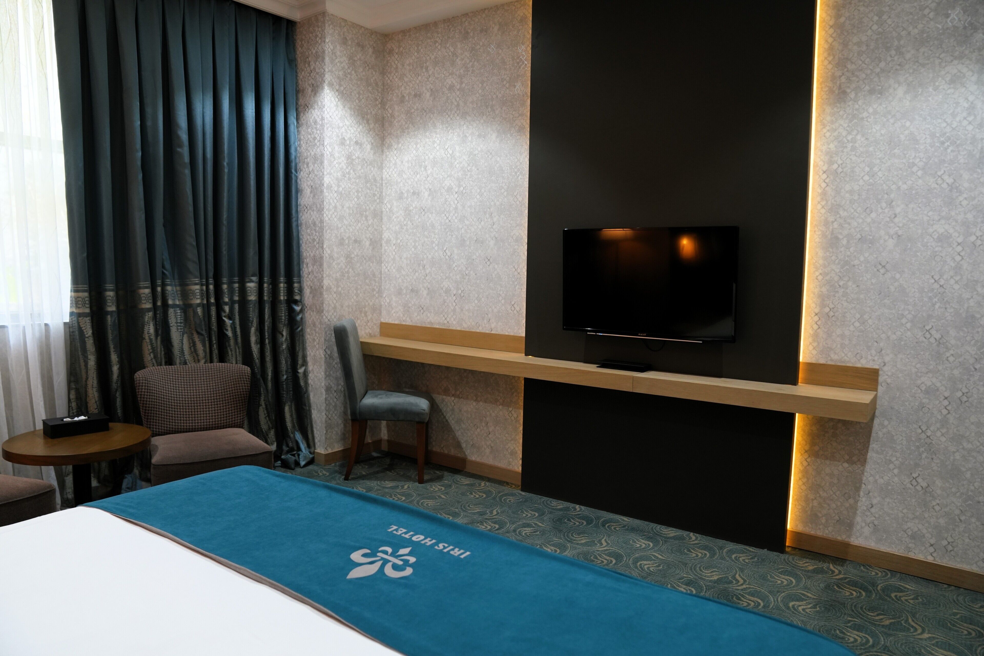 A hotel room with a bed, a television mounted on the wall, a desk, and a chair.