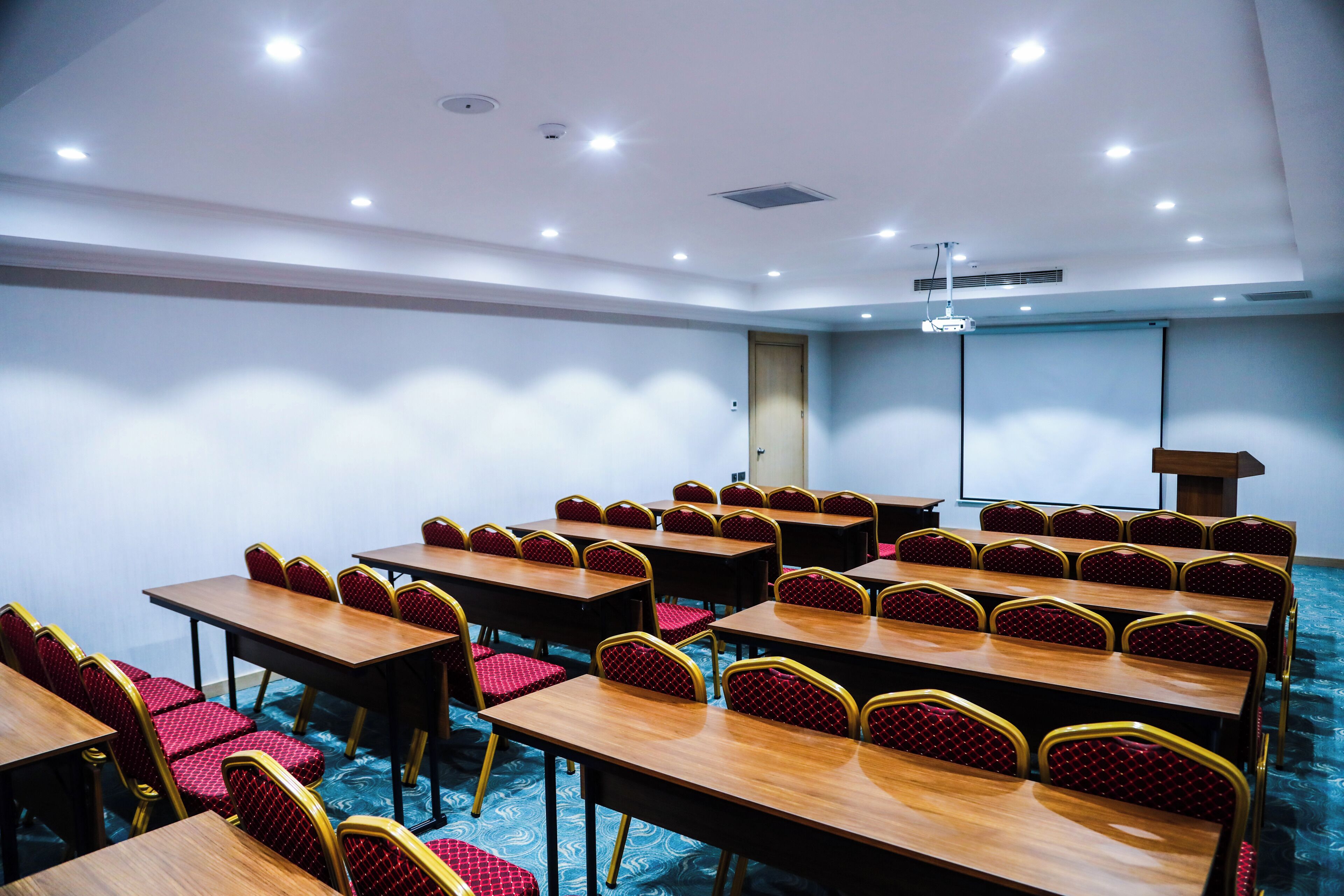 A conference room with multiple tables and chairs, a podium, and a projector screen.