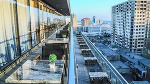 Un bâtiment moderne doté d’une terrasse sur le toit, aménagée avec des espaces de détente en plein air et des plantes en pot.
