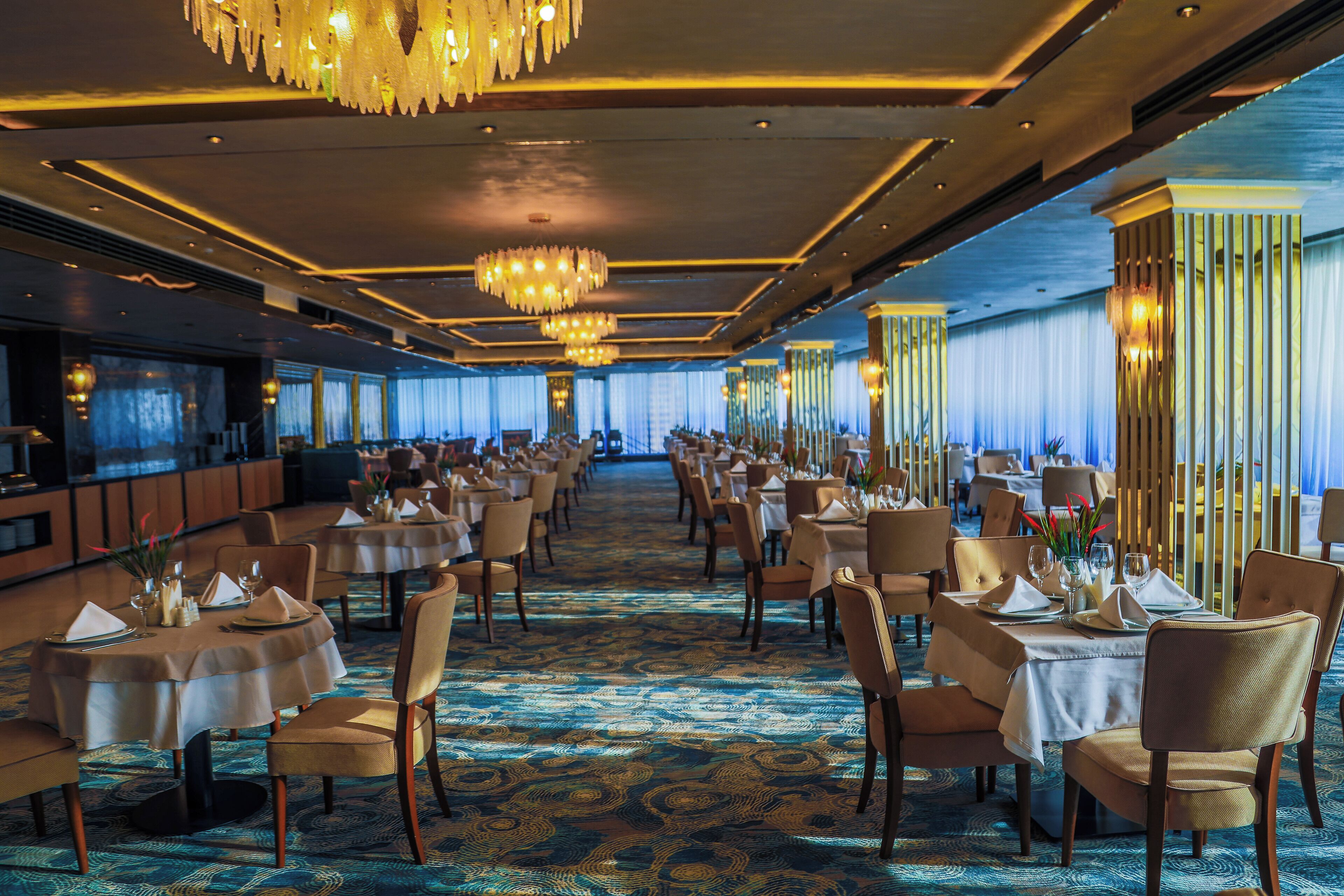 A spacious banquet hall with round tables, chairs, and chandeliers.