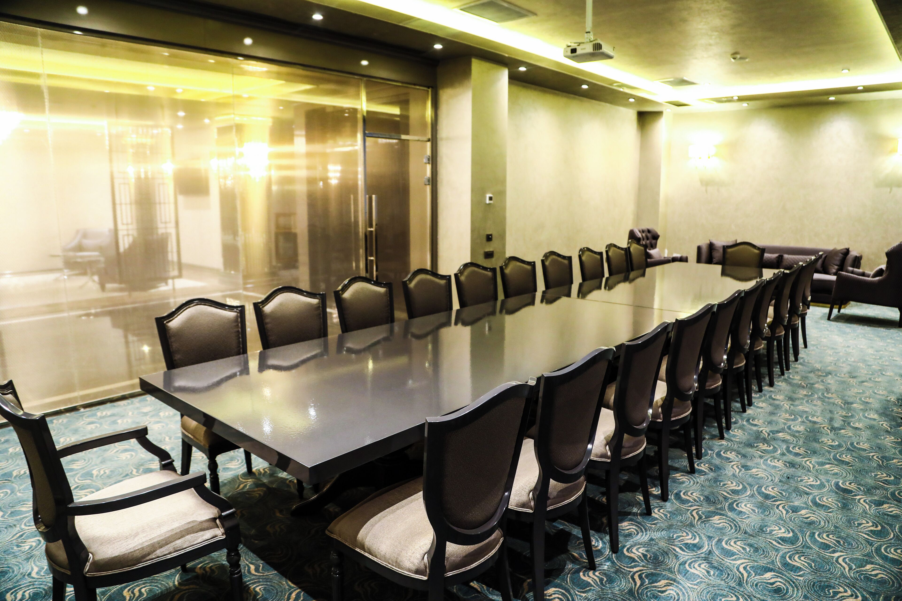 A conference room with a long table and chairs, a glass partition, and a patterned carpet.