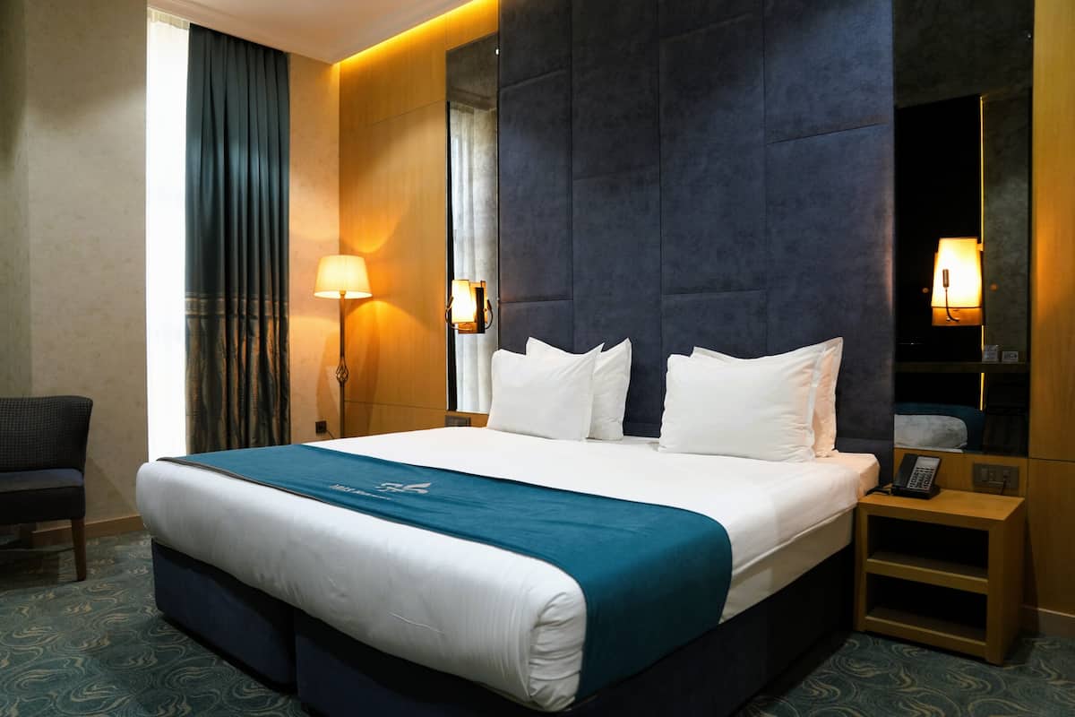 Habitación de hotel con una cama grande, una mesita de noche con teléfono, una silla y un espejo.
