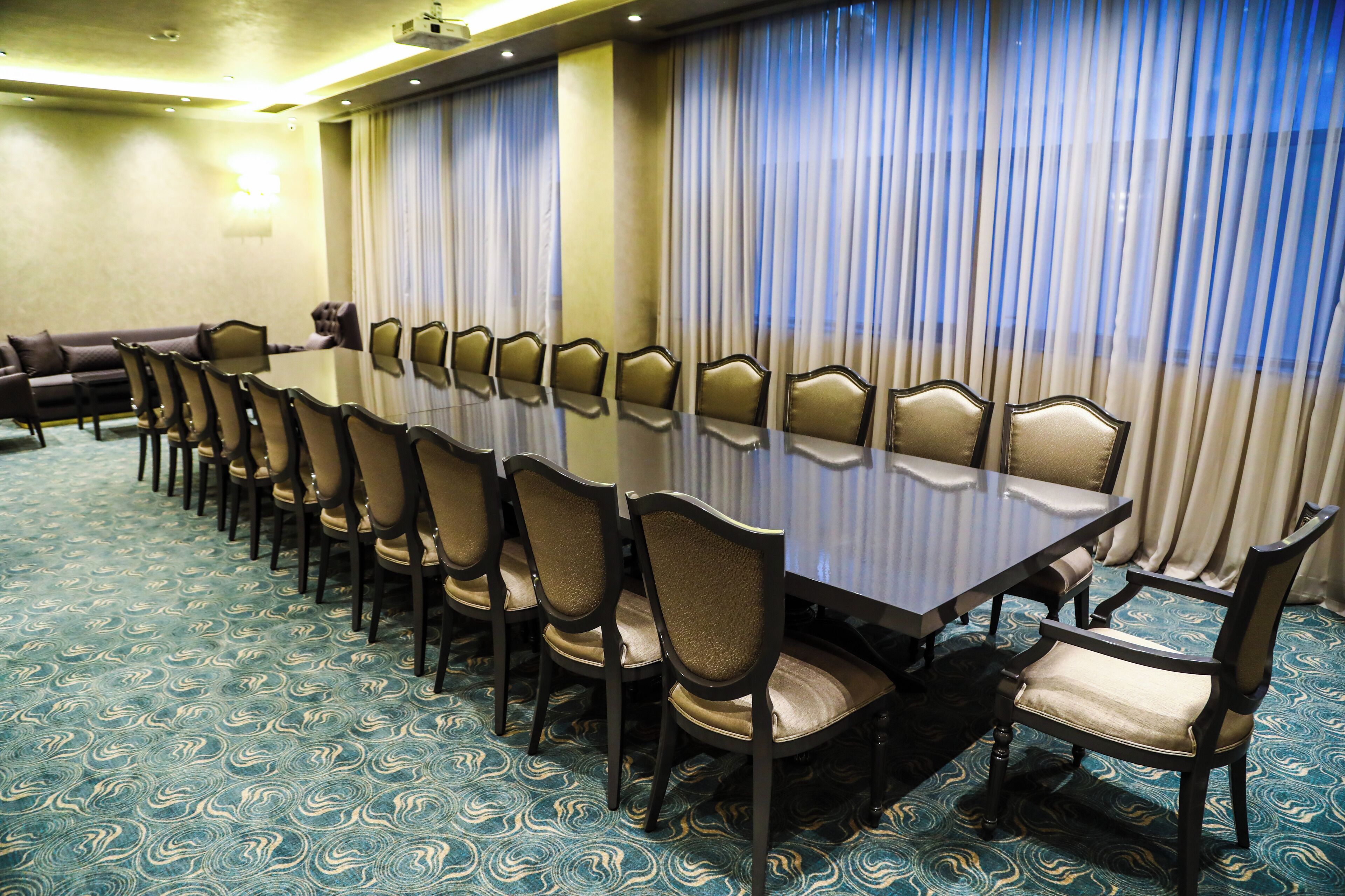 Une salle de conférence avec une longue table et des chaises, une moquette à motifs et des rideaux.