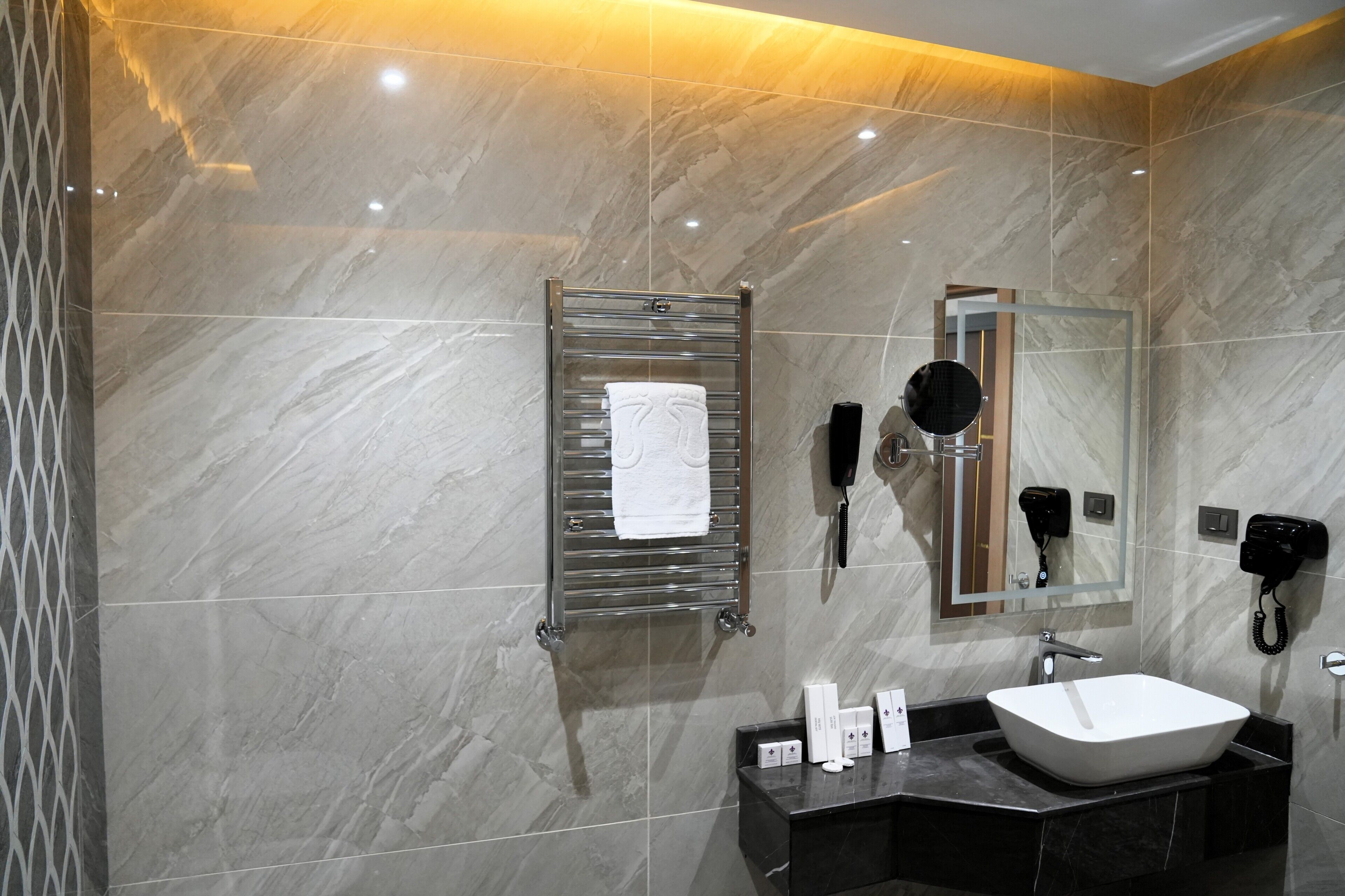 A modern bathroom with a marble wall, a towel rack, a sink, a mirror, and a hairdryer.