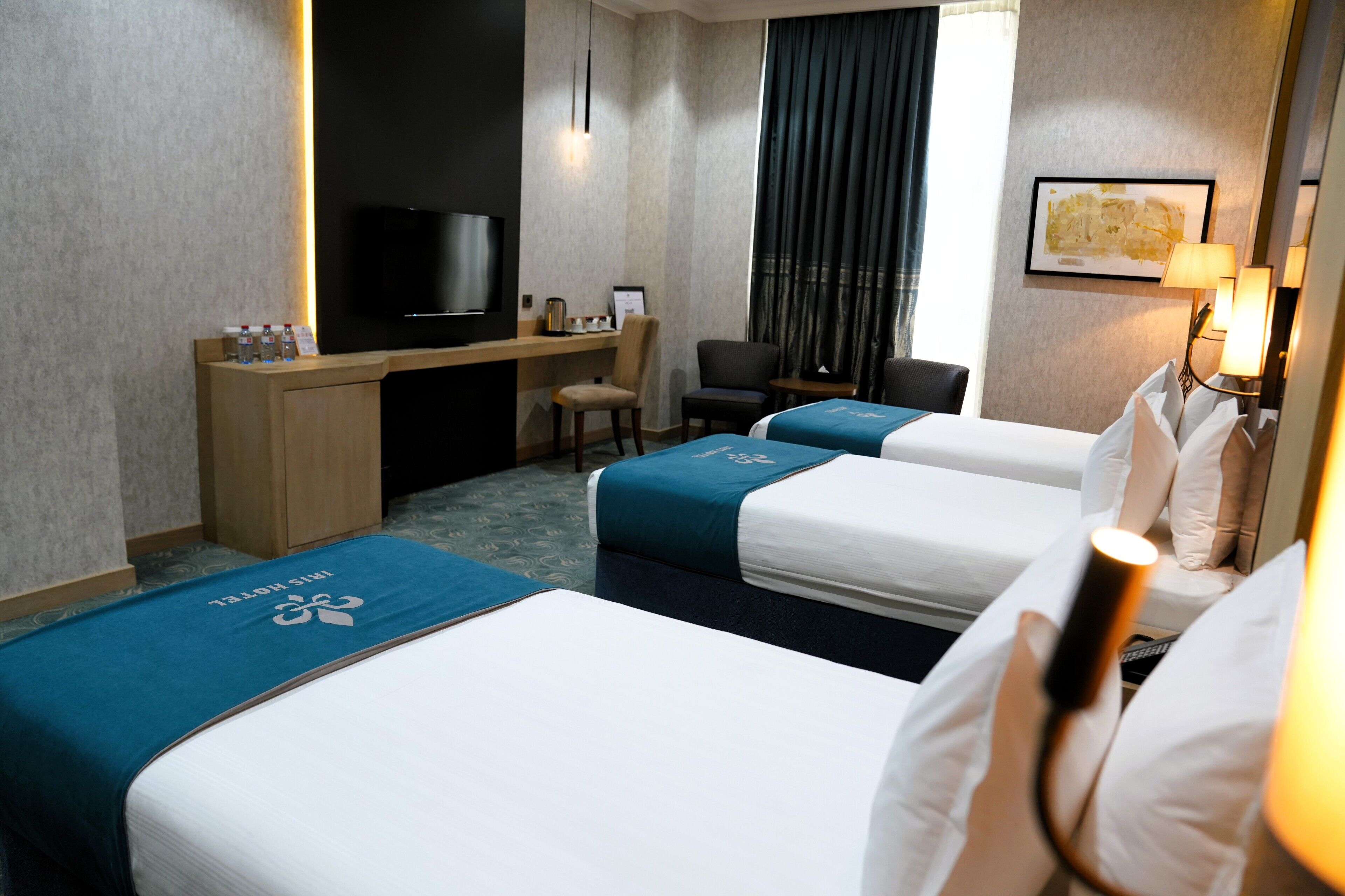 A hotel room with a desk, two beds, a TV, and a window with curtains.