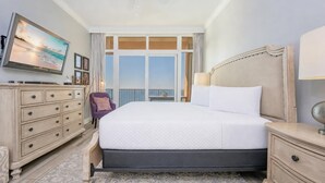 Habitación de hotel con cama, cómoda, silla, televisión y una ventana grande con vistas.
